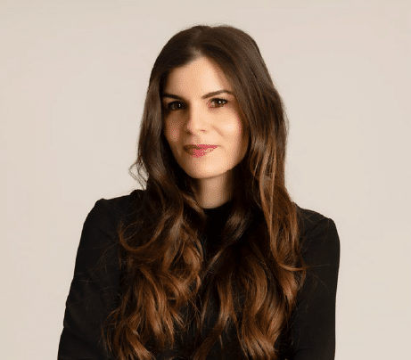 Adi Mor Sitelbah smiles at the camera with crossed arms. She has brown hair and wears a dark blouse in front of a light backdrop.