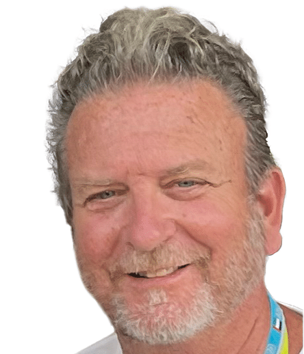 Sheldon Pollack smiles. He has grey hair and beard and is wearing a white t-shirt with a lanyard around his neck.